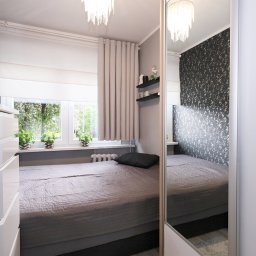 Bogusława Trela Fotografia - Nowoczesna sypialnia z szarą pościelą, wzorzystą tapetą, białymi meblami i lustrzanym frontem szafy przesuwnej, oświetlona lampą kryształową