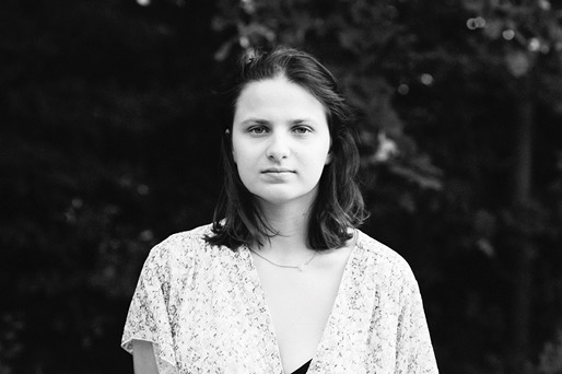 Portret czarno-biały kobiety z krótkimi włosami, w kwiecistej bluzce, na tle ciemnej zieleni.