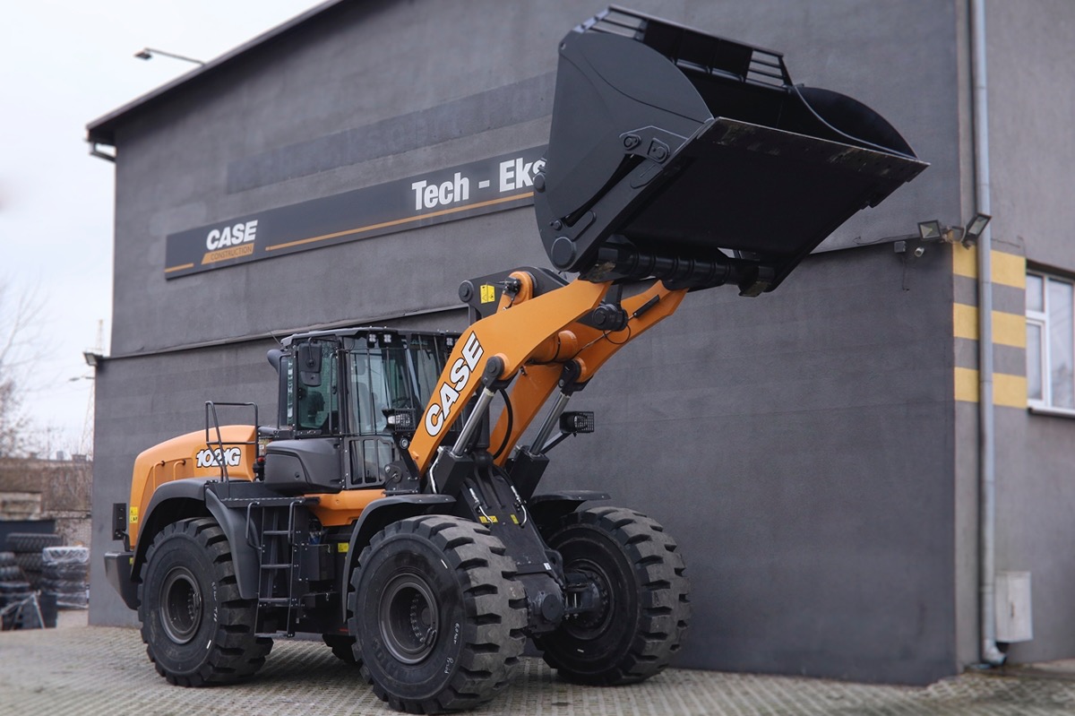Pomarańczowo-czarna ładowarka kołowa Case 1021G na tle szarego budynku z logo firmy Tech-Eks.