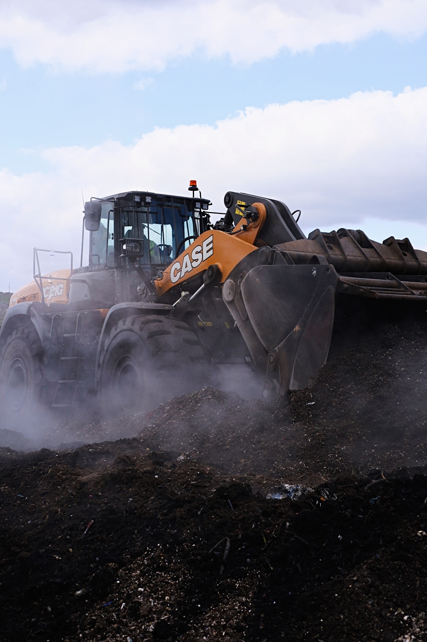 Ładowarka kołowa CASE nabiera ziemię, unosząc tumany kurzu, na tle pochmurnego nieba.