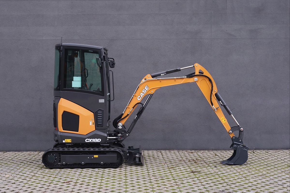 Mała koparka CASE CX18D na gąsienicach, z żółtym ramieniem i łyżką, stojąca na betonowej kostce brukowej na tle szarej ściany.