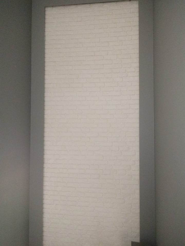 Wnęka w szarej ścianie wyłożona białą cegłą dekoracyjną, imitującą mur, z delikatnym cieniowaniem między cegłami.