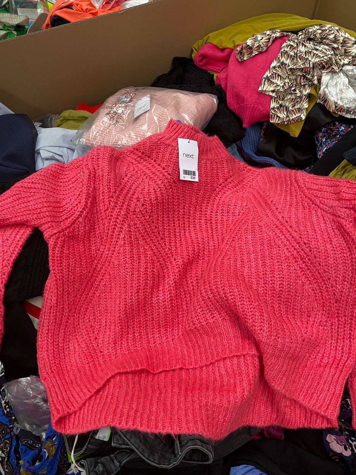 Różowy sweter z metką firmy Next leży w kartonie z innymi ubraniami w London.