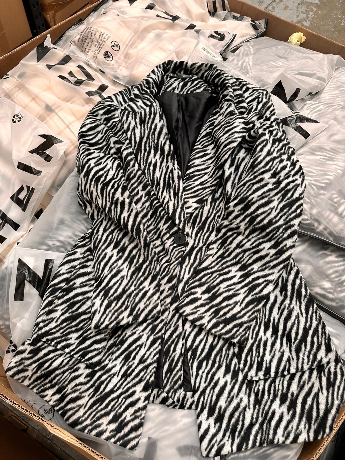 Czarno-biały płaszcz w zebrę leżący na kartonie z plastikowymi torbami z logo marki odzieżowej.