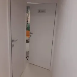 Dwie białe, minimalistyczne drzwi wewnętrzne w korytarzu, jedne otwarte ukazujące wnętrze gabinetu z fototapetą leśną.