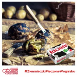 Pieczone ziemniaki z masłem na brązowym papierze, jeden ziemniak przekrojony z wbitym nożem, obok kostka masła Faciate, w tle rozmyte ziemniaki i koszyk.