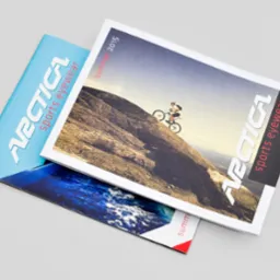 Dwa katalogi produktowe firmy Arctica Sports Eyewear, jeden z motywem górskim i rowerzystą, drugi z motywem morskim, leżące na szarym tle.