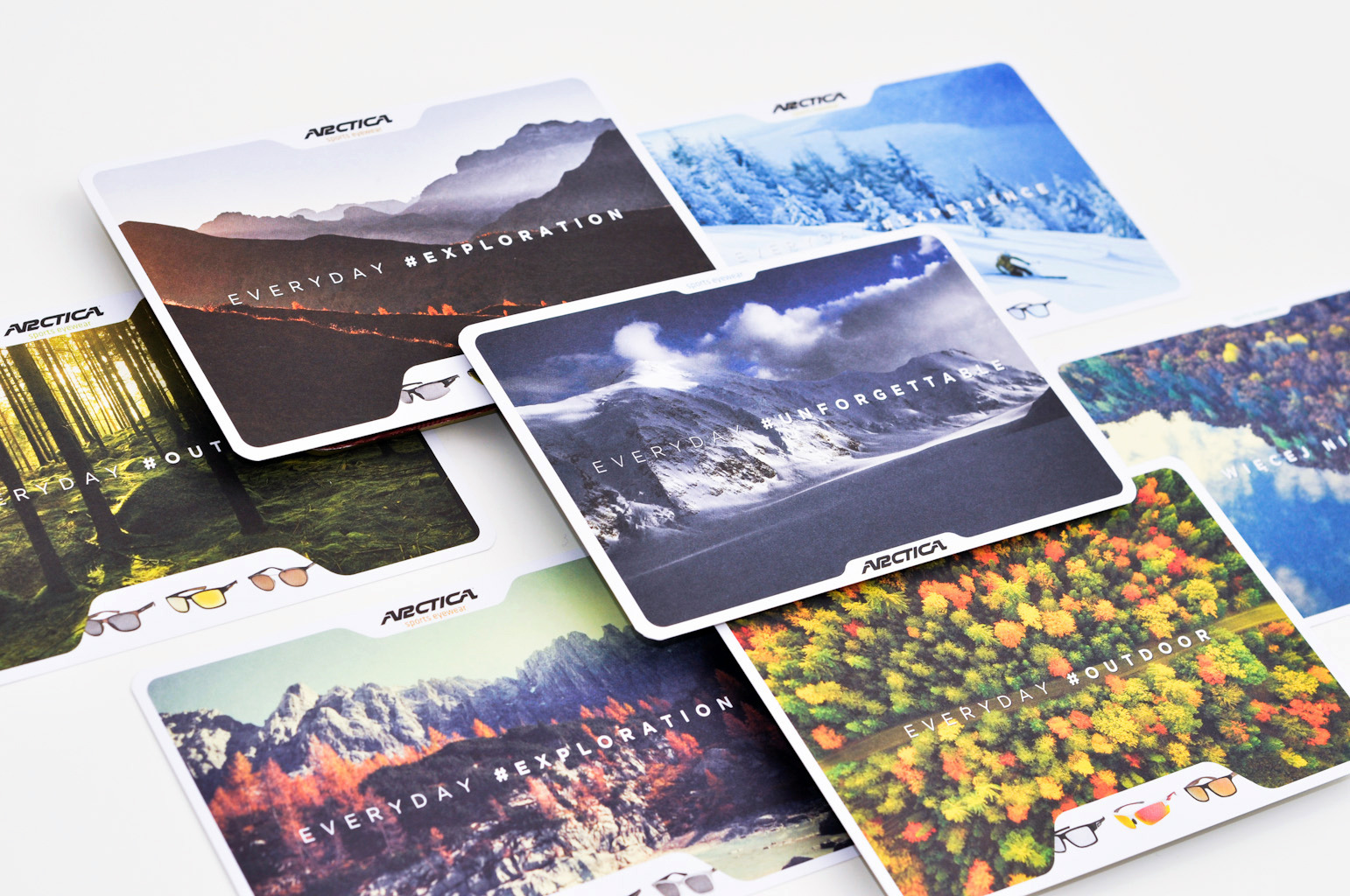 Zestaw wizytówek firmy Arctica z fotografiami gór, lasów i tekstami 'Everyday #Exploration', 'Everyday #Outdoor', 'Everyday #Unforgettable', prezentujących logo firmy i różne modele okularów.