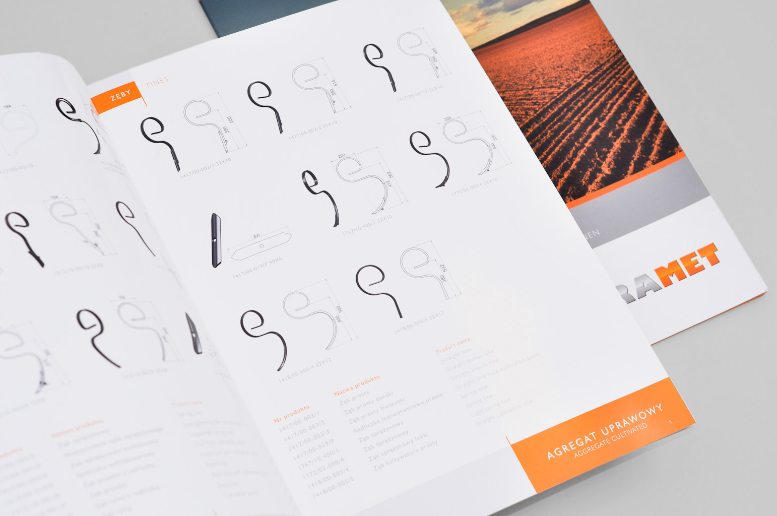 Otwarta broszura reklamowa z ilustracjami i technicznymi rysunkami zębów do agregatów uprawowych, obok leży zamknięta broszura z pomarańczowym logo firmy Ramet i zdjęciem zaoranego pola w tle.