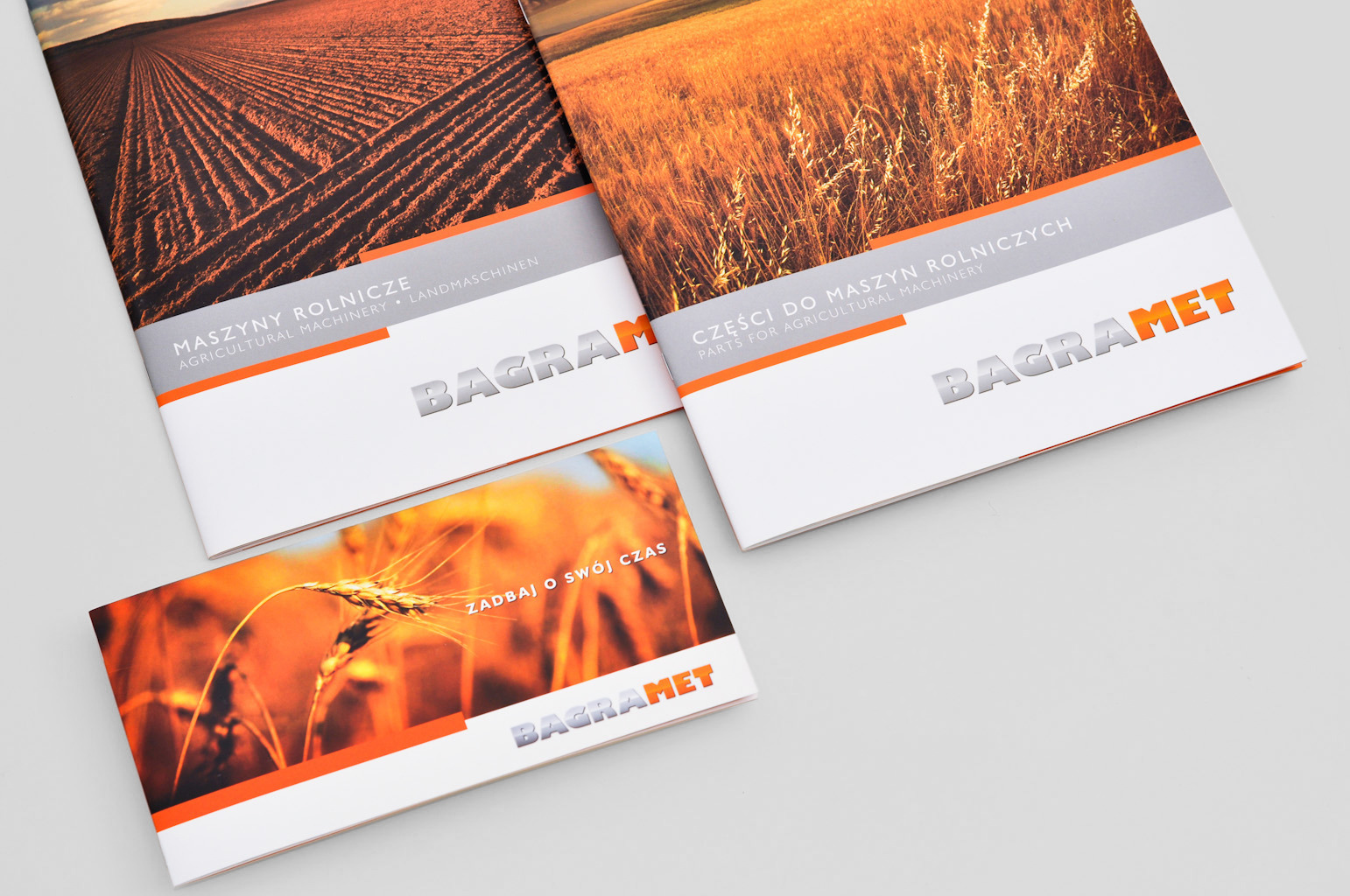 Trzy ulotki reklamowe firmy Bagramet z motywami rolniczymi: pole uprawne, kłosy zbóż i hasło 'Zadbaj o swój czas', leżące na szarym tle.
