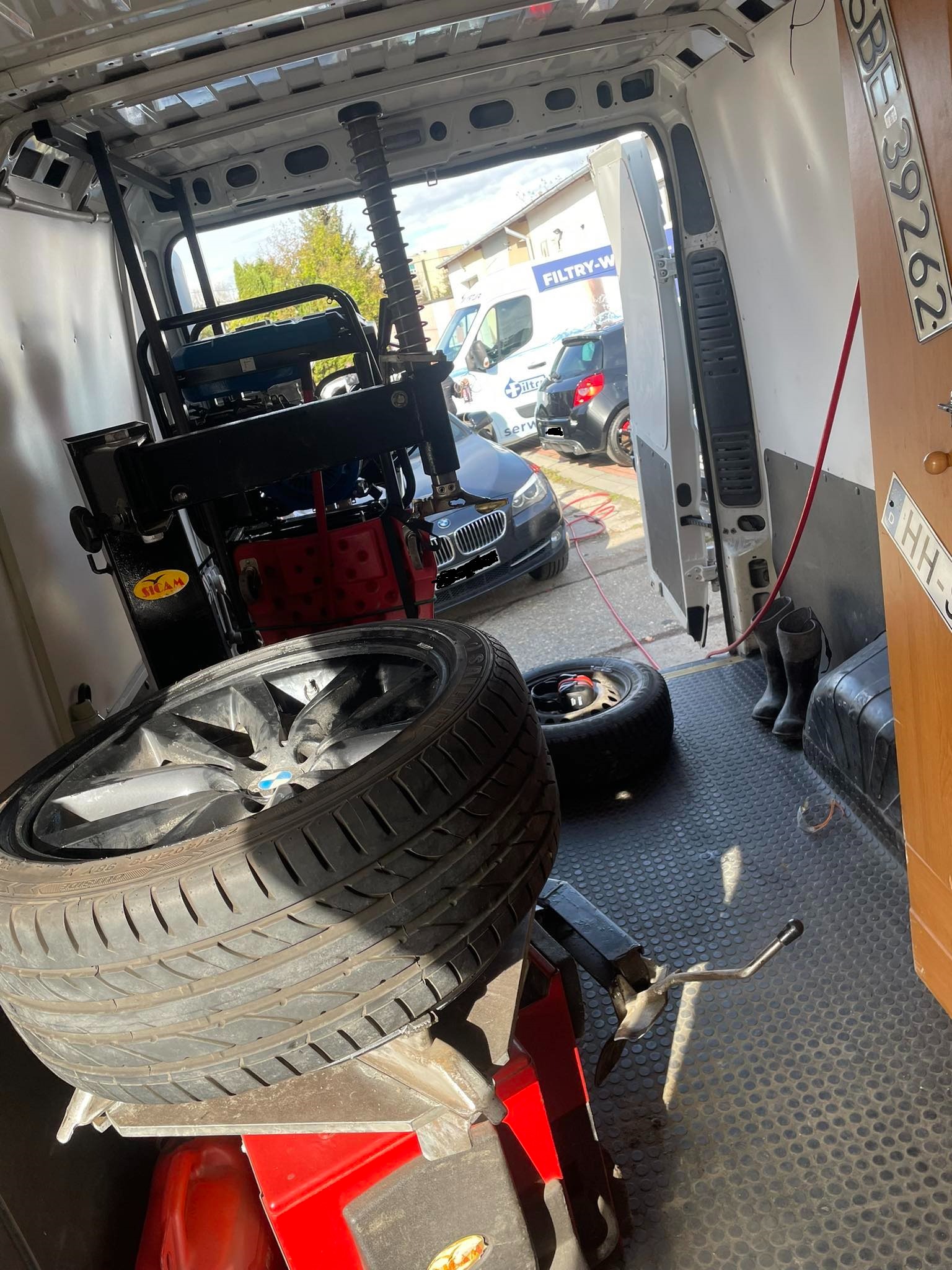 Opona samochodowa na montażownicy wewnątrz mobilnego warsztatu, z widocznym fragmentem samochodu klienta na zewnątrz