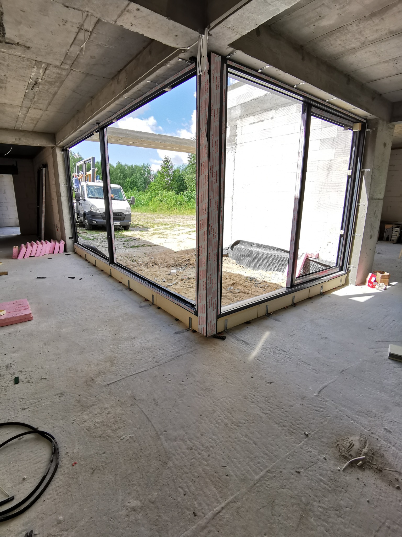 Montaż okien w surowym stanie budynku, widoczny podnośnik i samochód dostawczy na zewnątrz.