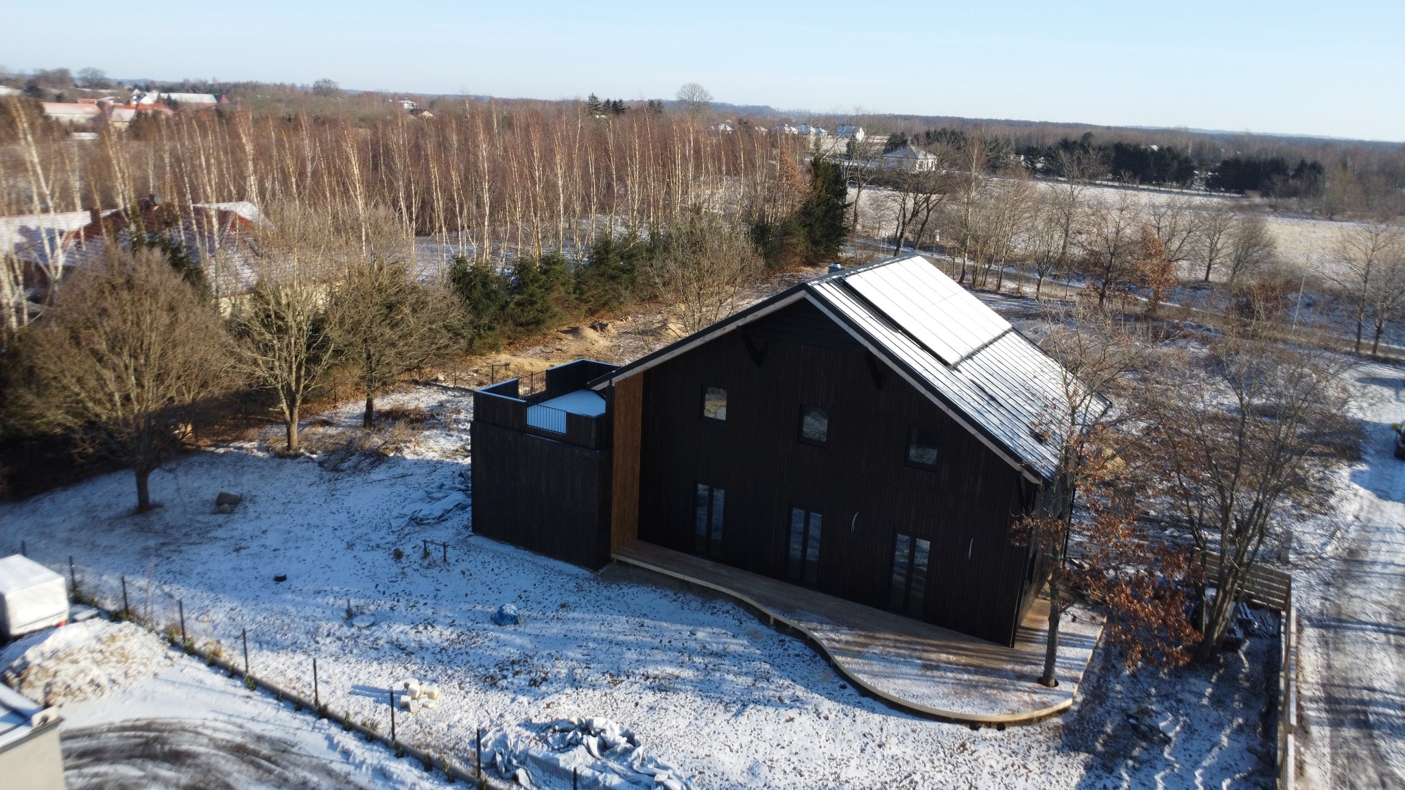Nowoczesny, ciemny dom z panelami słonecznymi na dachu, otoczony zimowym krajobrazem. Widok z lotu ptaka ukazuje unikalny projekt i otoczenie.