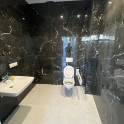 Usługi Remontowo Budowlane Kamil Krawczyk - Nowoczesna łazienka w trakcie wykańczania z czarnymi płytkami imitującymi marmur na ścianach i jasnymi płytkami na podłodze. Widoczna umywalka, toaleta z podwieszanym systemem spłukiwania...