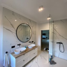 Usługi Remontowo Budowlane Kamil Krawczyk - Nowoczesna łazienka z marmurowymi płytkami, owalnymi umywalkami nablatowymi i czarną armaturą, uzupełniona okrągłym lustrem i kabiną prysznicową typu walk-in.