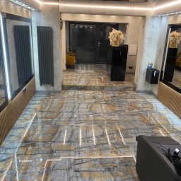 Usługi Remontowo Budowlane Kamil Krawczyk - Wnętrze salonu z marmurową podłogą w odcieniach szarości i brązu, oświetleniem LED wzdłuż krawędzi płytek, grzejnikami w kolorze antracytowym i elementami dekoracyjnymi.