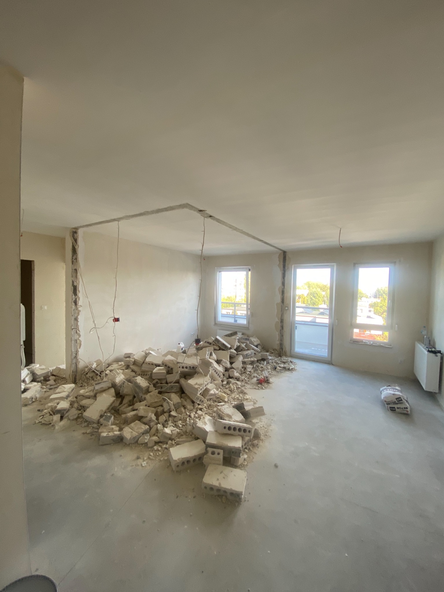 Wnętrze mieszkania w trakcie demontażu ścian działowych, widoczny gruz, odsłonięte przewody elektryczne i przygotowane podłoże pod dalsze prace wykończeniowe.