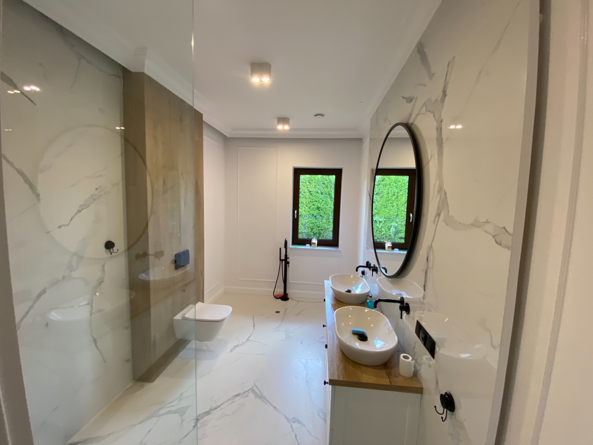 Nowoczesna łazienka z marmurowymi płytkami, podwójną umywalką nablatową i kabiną prysznicową typu walk-in.