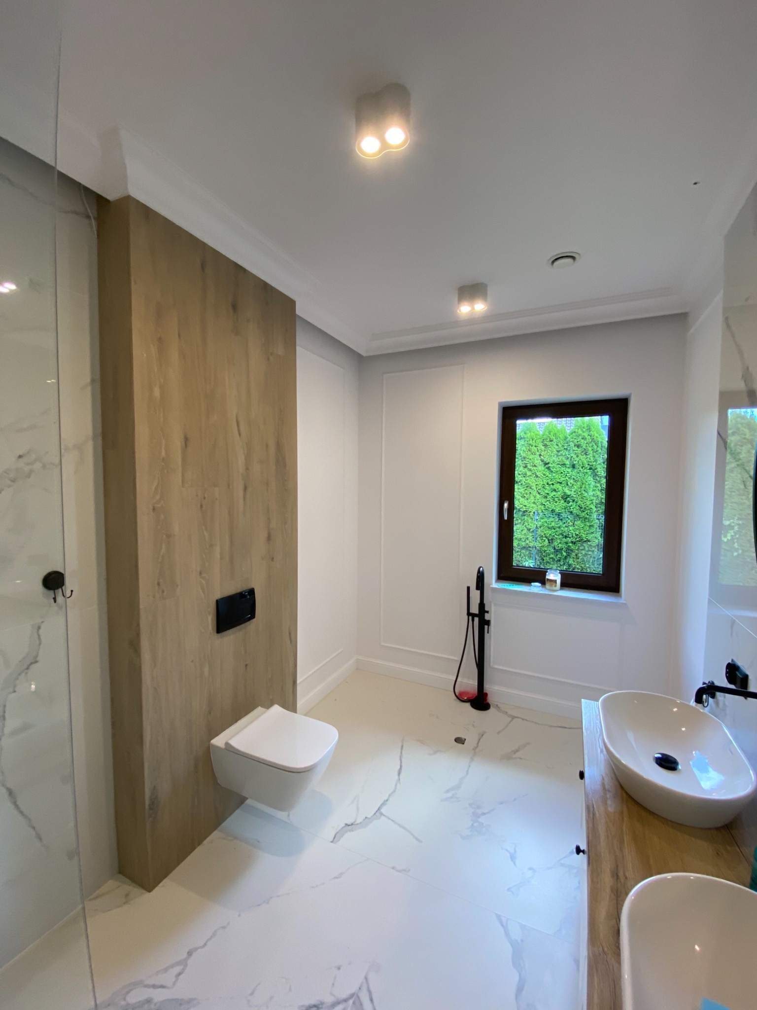 Nowoczesna łazienka z płytkami imitującymi marmur, drewnianą zabudową toalety podtynkowej i umywalkami nablatowymi, widok z góry.