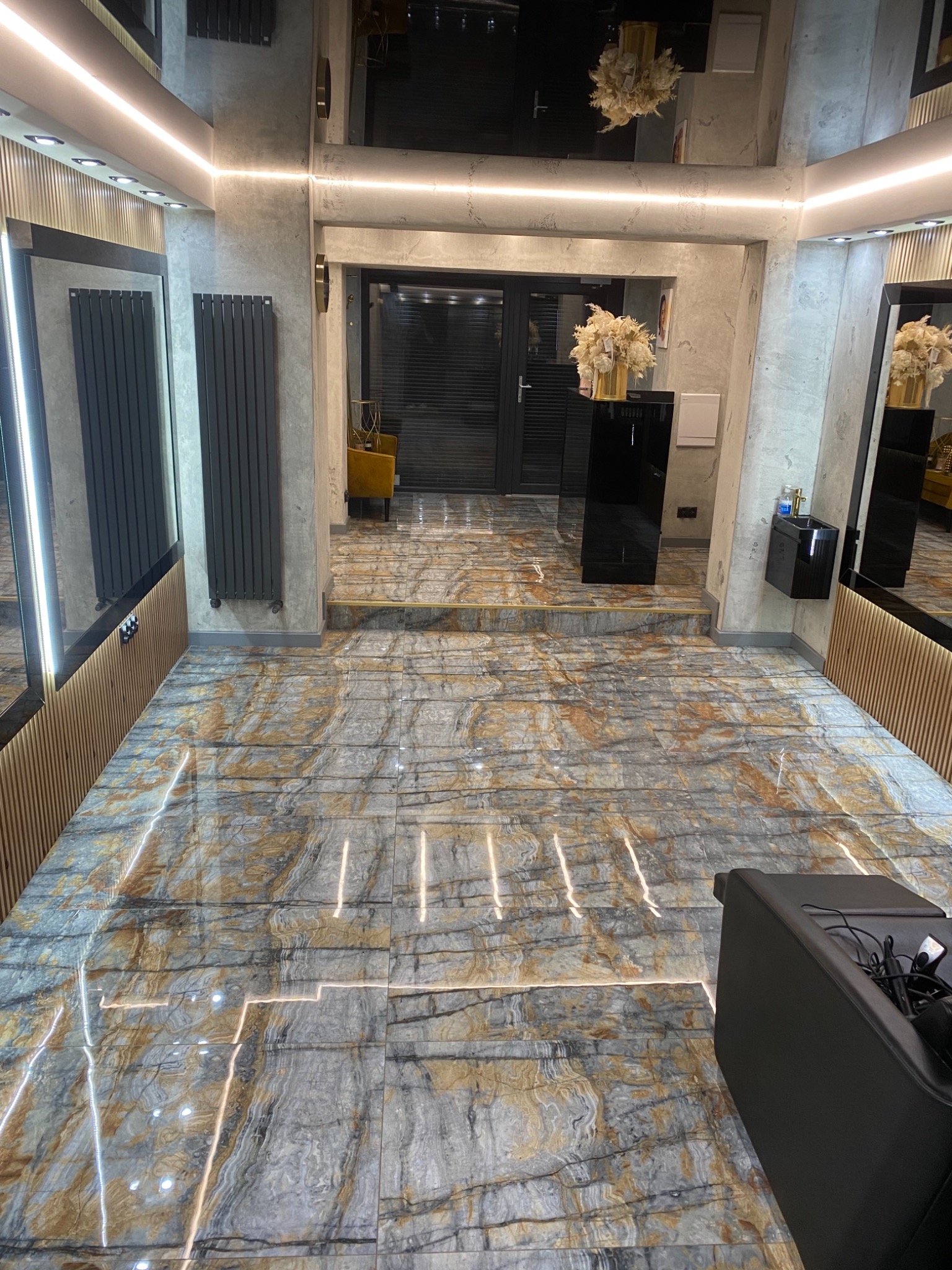 Wnętrze salonu z marmurową podłogą w odcieniach szarości i brązu, oświetleniem LED wzdłuż krawędzi płytek, grzejnikami w kolorze antracytowym i elementami dekoracyjnymi.