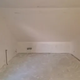 Poddasze po wstępnym wyrównaniu ścian i podłogi, widoczny stołek malarski i fragment okna