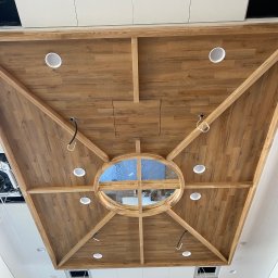 WRONA Usługi Remontowo Wykończeniowe Kacper Wrona - Drewniany sufit kasetonowy z okrągłym świetlikiem i wbudowanym oświetleniem punktowym. Widok z dołu, elementy instalacji elektrycznej widoczne.