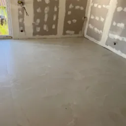 Jasne płytki podłogowe imitujące marmur w pomieszczeniu z przygotowanymi ścianami do dalszych prac wykończeniowych. Widoczne kable elektryczne.