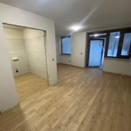 Wnętrze mieszkania w trakcie remontu: ułożona podłoga z paneli drewnopodobnych, przygotowana do wykończenia łazienka z widoczną instalacją hydrauliczną, okna i drzwi zabezpieczone folią.