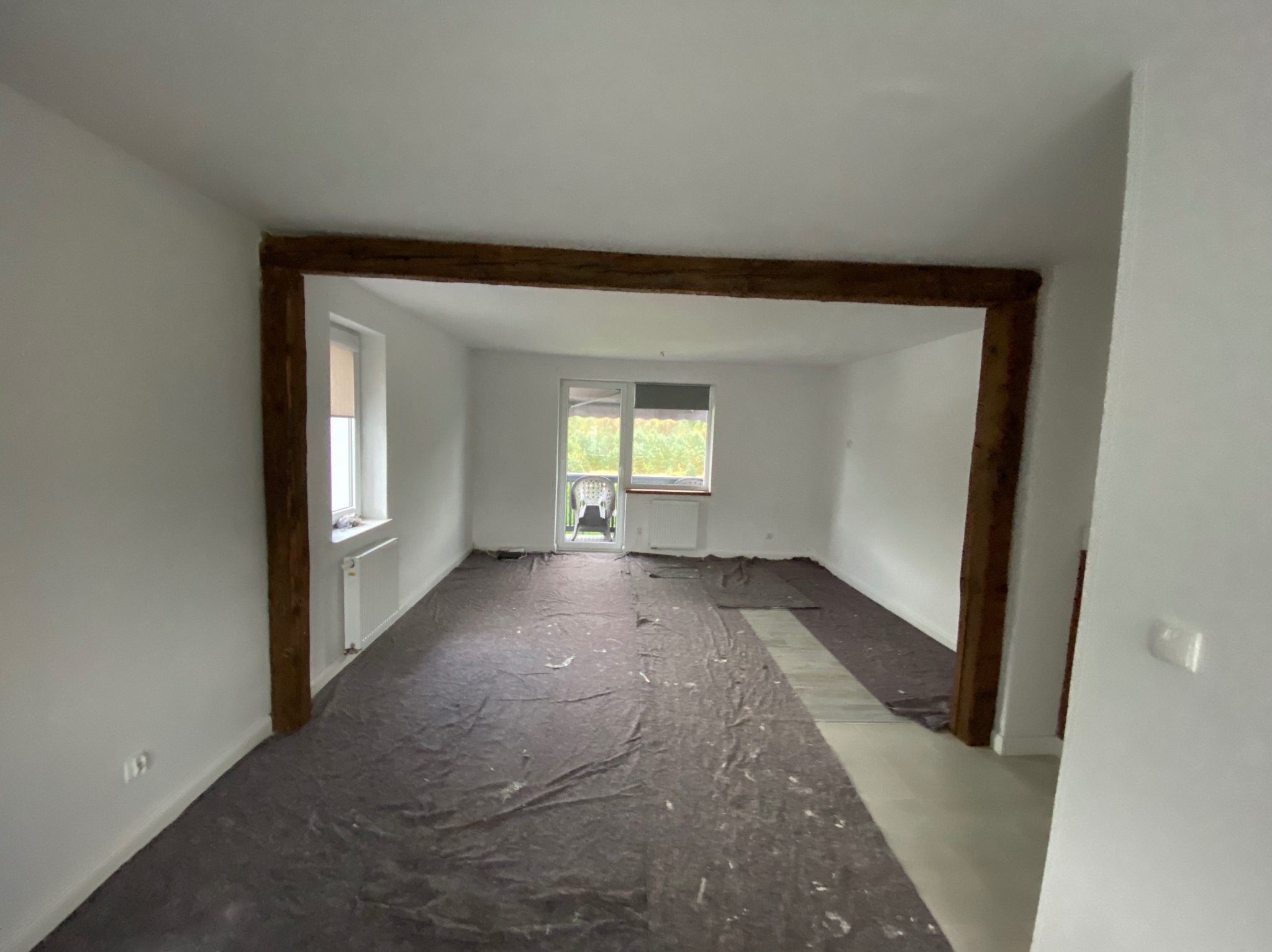 Pokój w trakcie prac przygotowawczych: podłoga zabezpieczona folią, ściany świeżo pomalowane na biało, widoczne drewniane elementy konstrukcyjne.