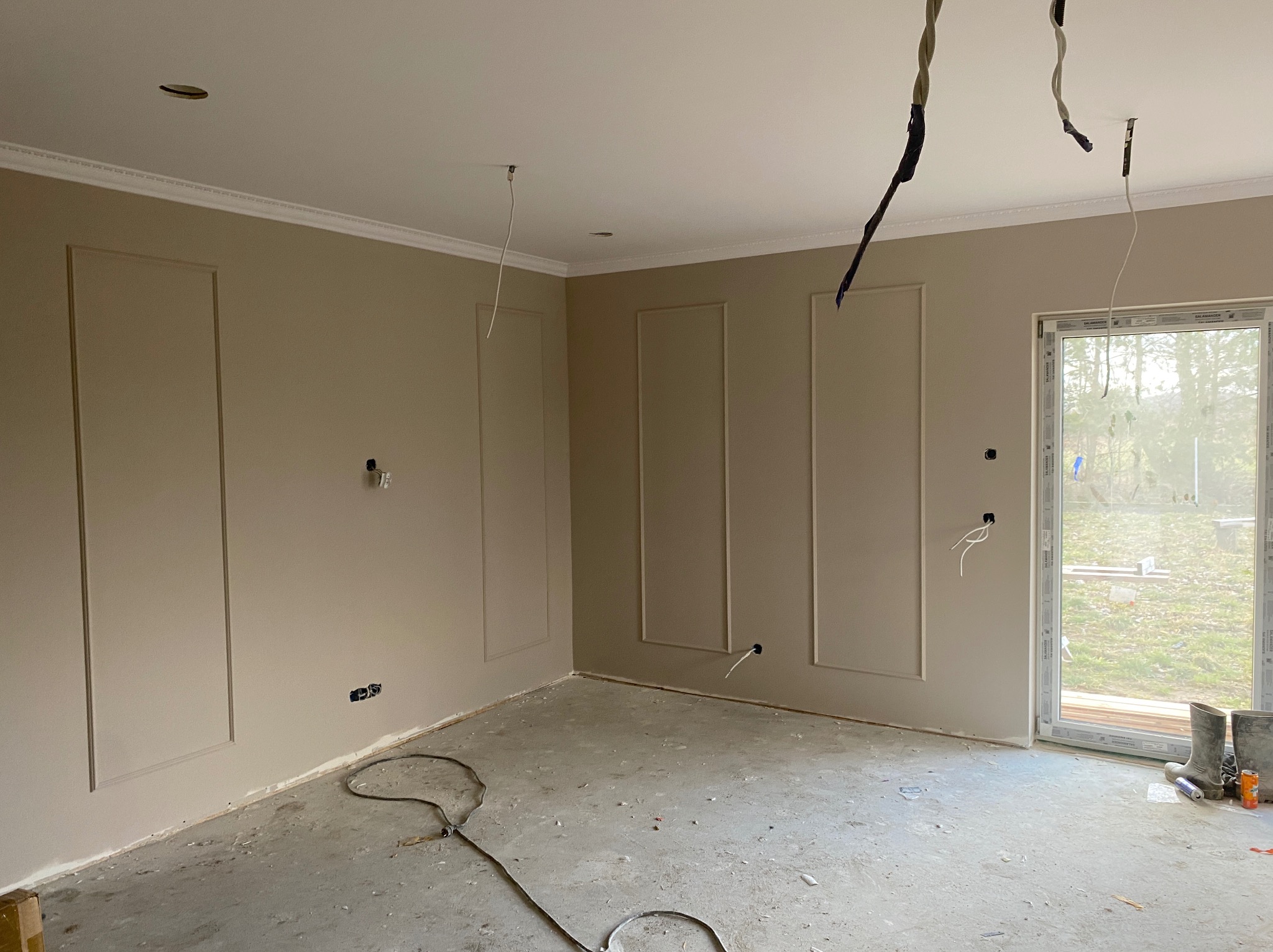 Pokój po malowaniu ścian na beżowo z dekoracyjnymi panelami i listwami przysufitowymi. Widoczne wystające kable i gumofilce przy oknie.