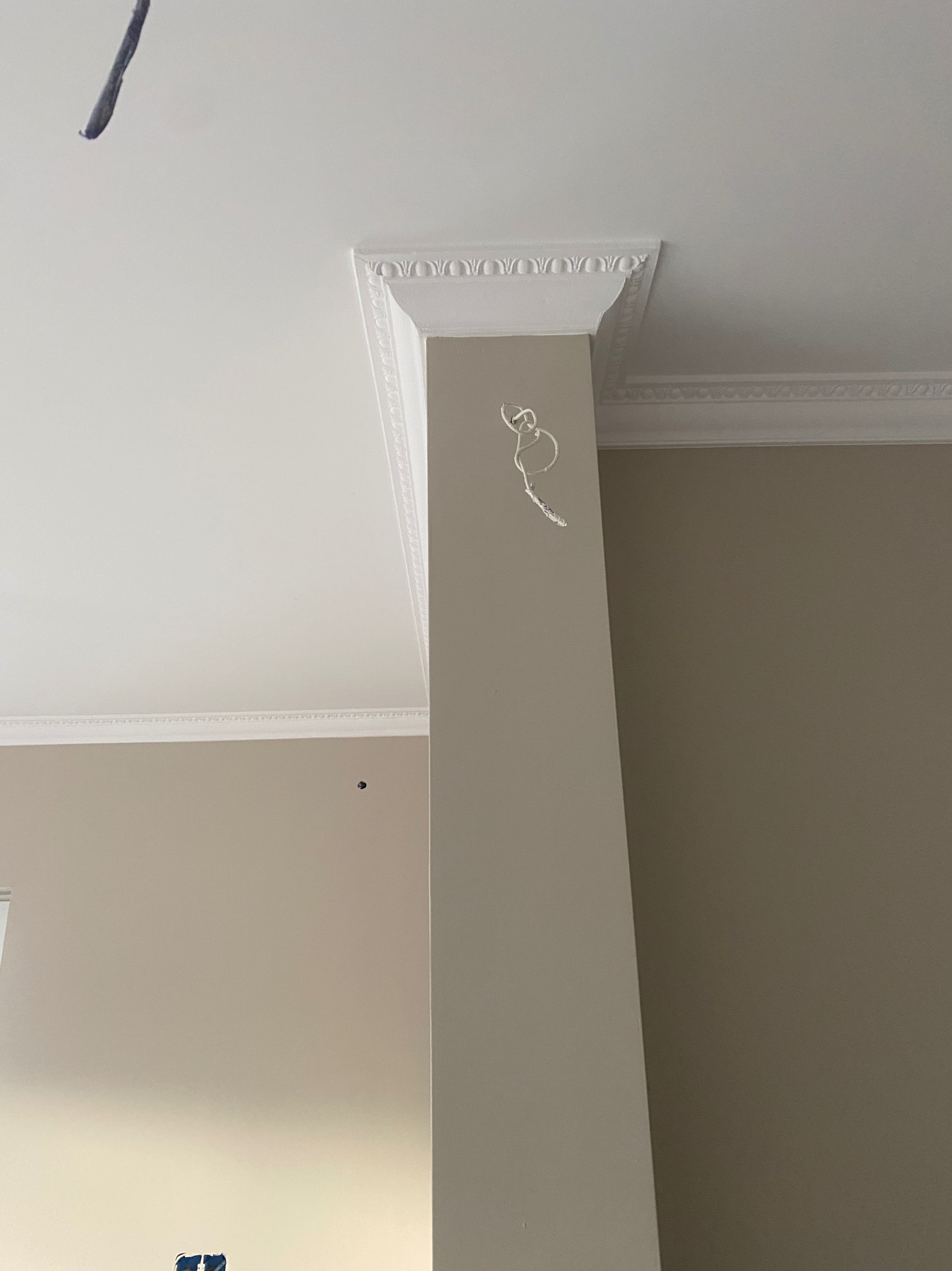 Wnętrze z kolumną zdobioną sztukaterią i gładzią, widoczne listwy dekoracyjne pod sufitem, ściany w odcieniach beżu, przygotowane do dalszych prac wykończeniowych.