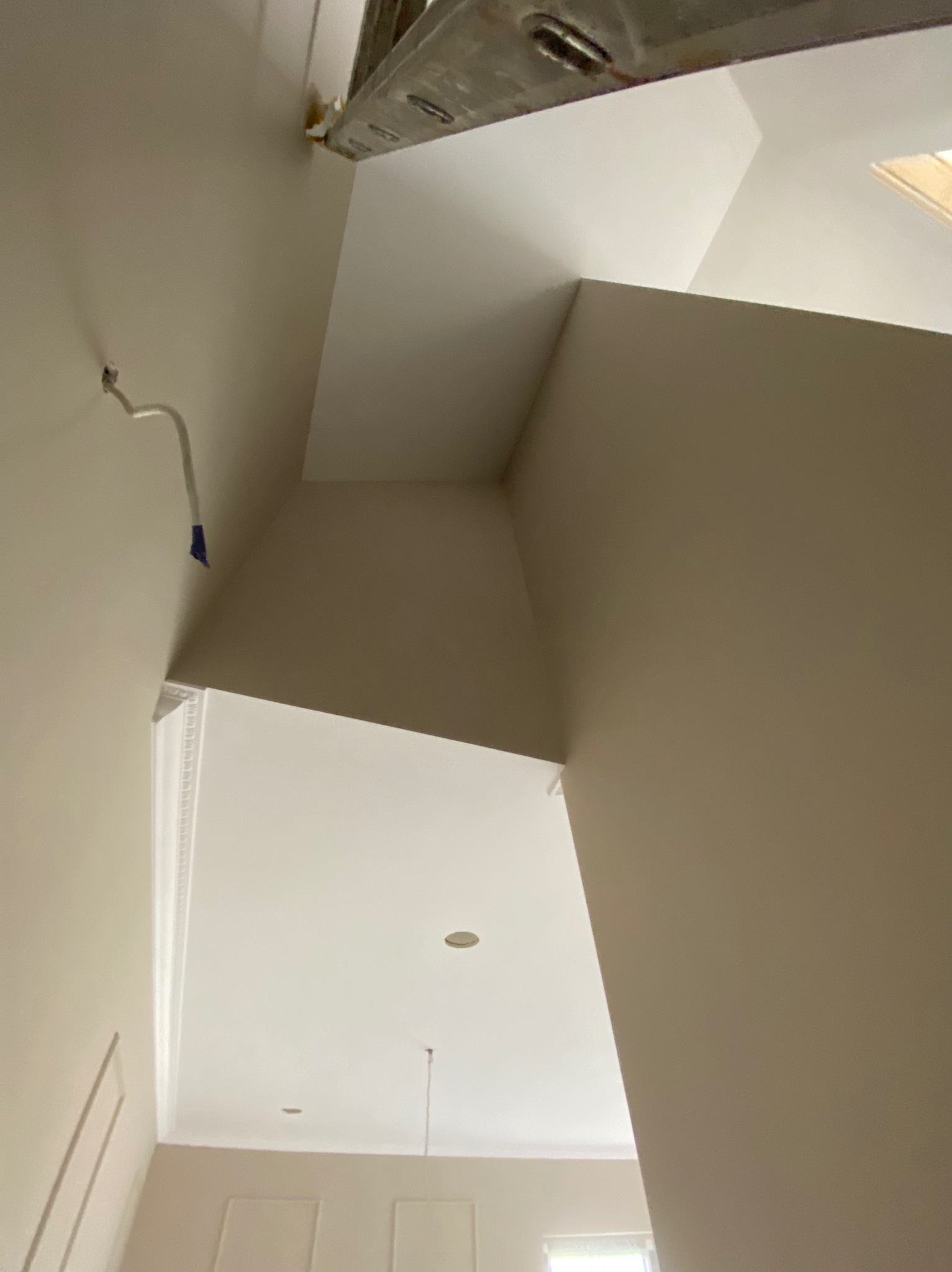 Pomieszczenie po malowaniu, jasne ściany i sufit, widoczne elementy dekoracyjne i fragment drabiny malarskiej. Świeżo pomalowane wnętrze z detalami wykończeniowymi.