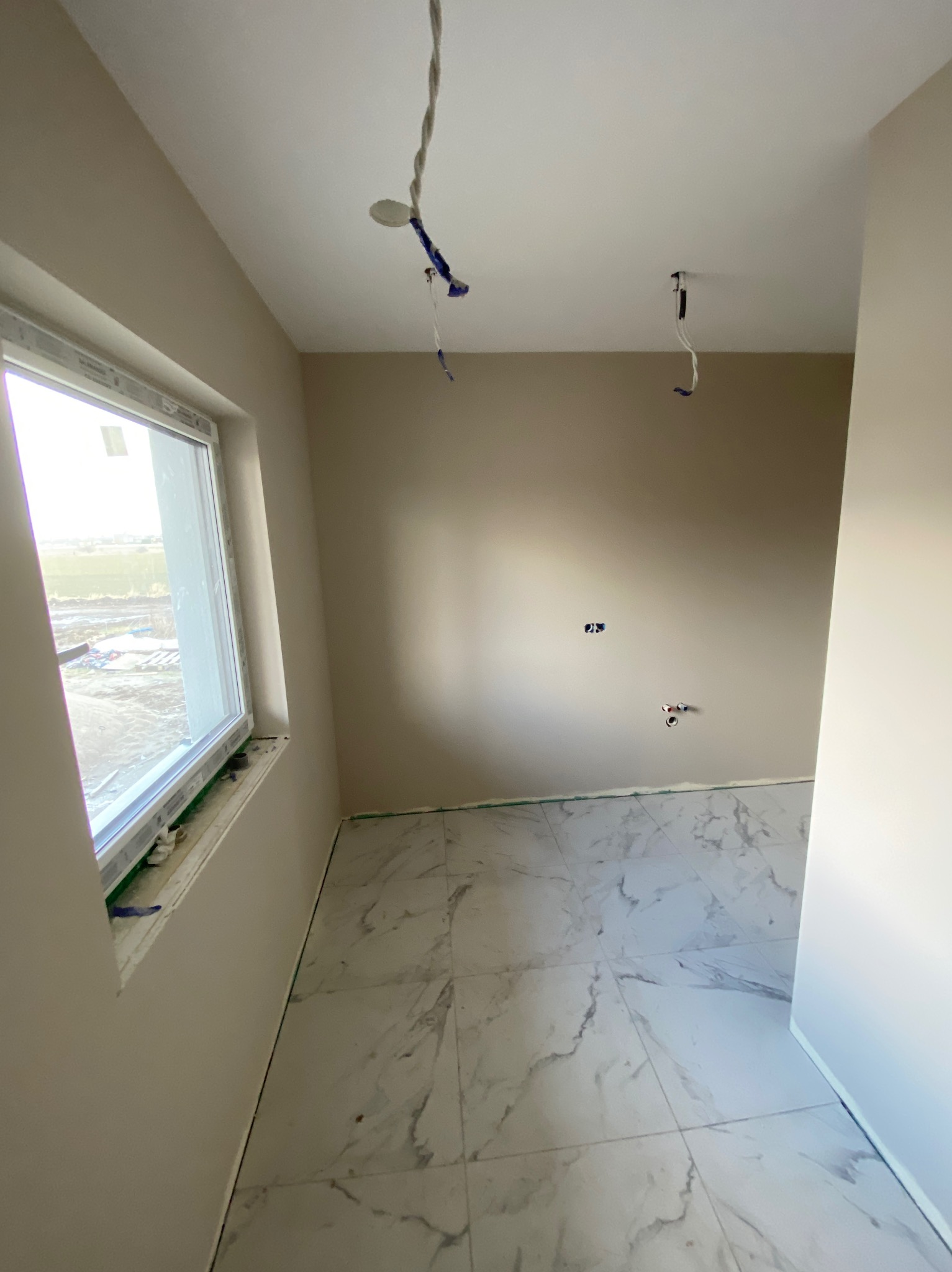 Jasna łazienka w trakcie wykańczania: marmurowe płytki podłogowe, świeżo pomalowane ściany w odcieniach beżu, widoczne instalacje elektryczne i hydrauliczne.