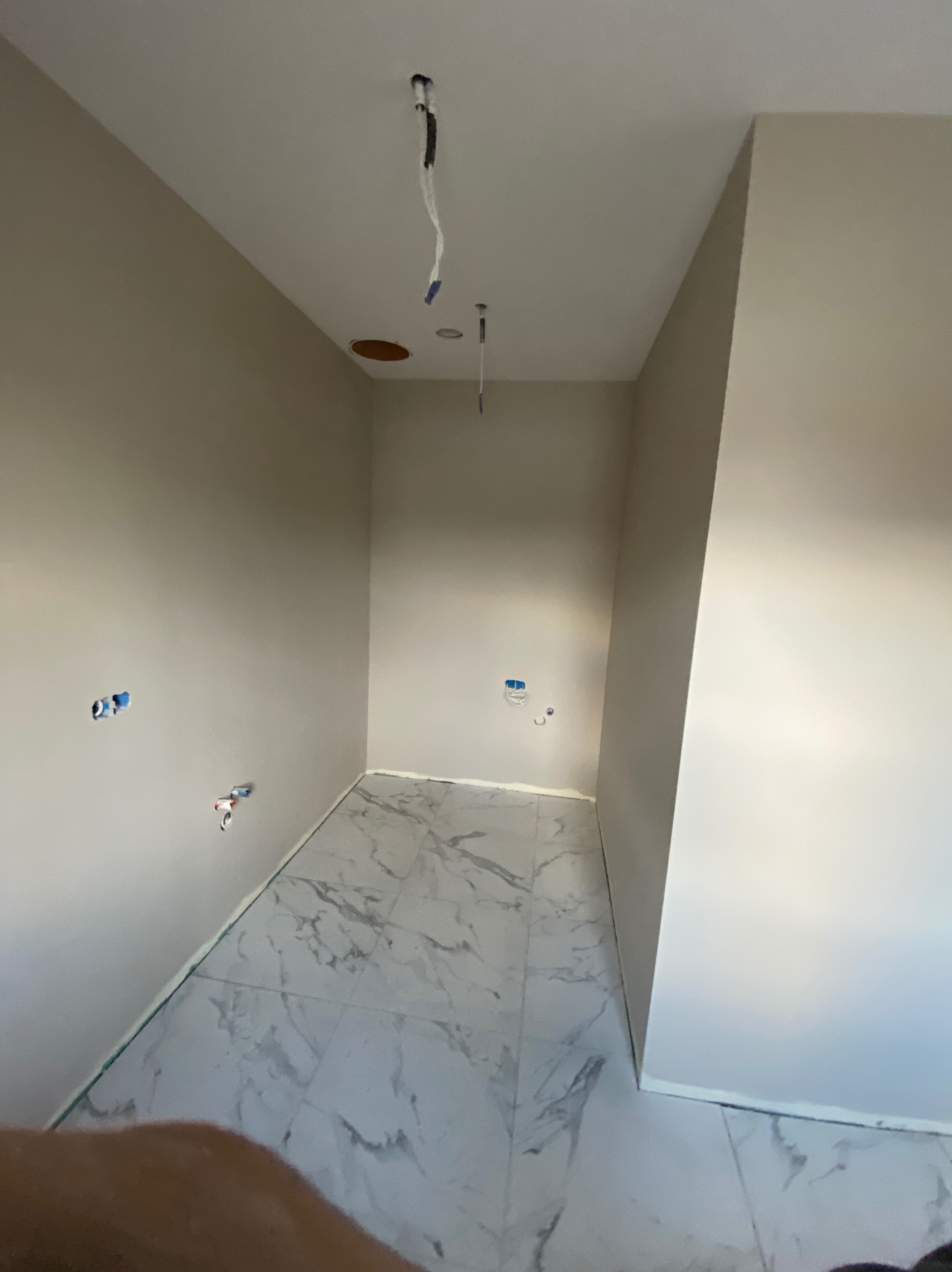 Jasna łazienka w trakcie prac wykończeniowych: marmurowe płytki podłogowe, świeżo pomalowane ściany w odcieniach beżu, widoczne instalacje elektryczne i hydrauliczne.