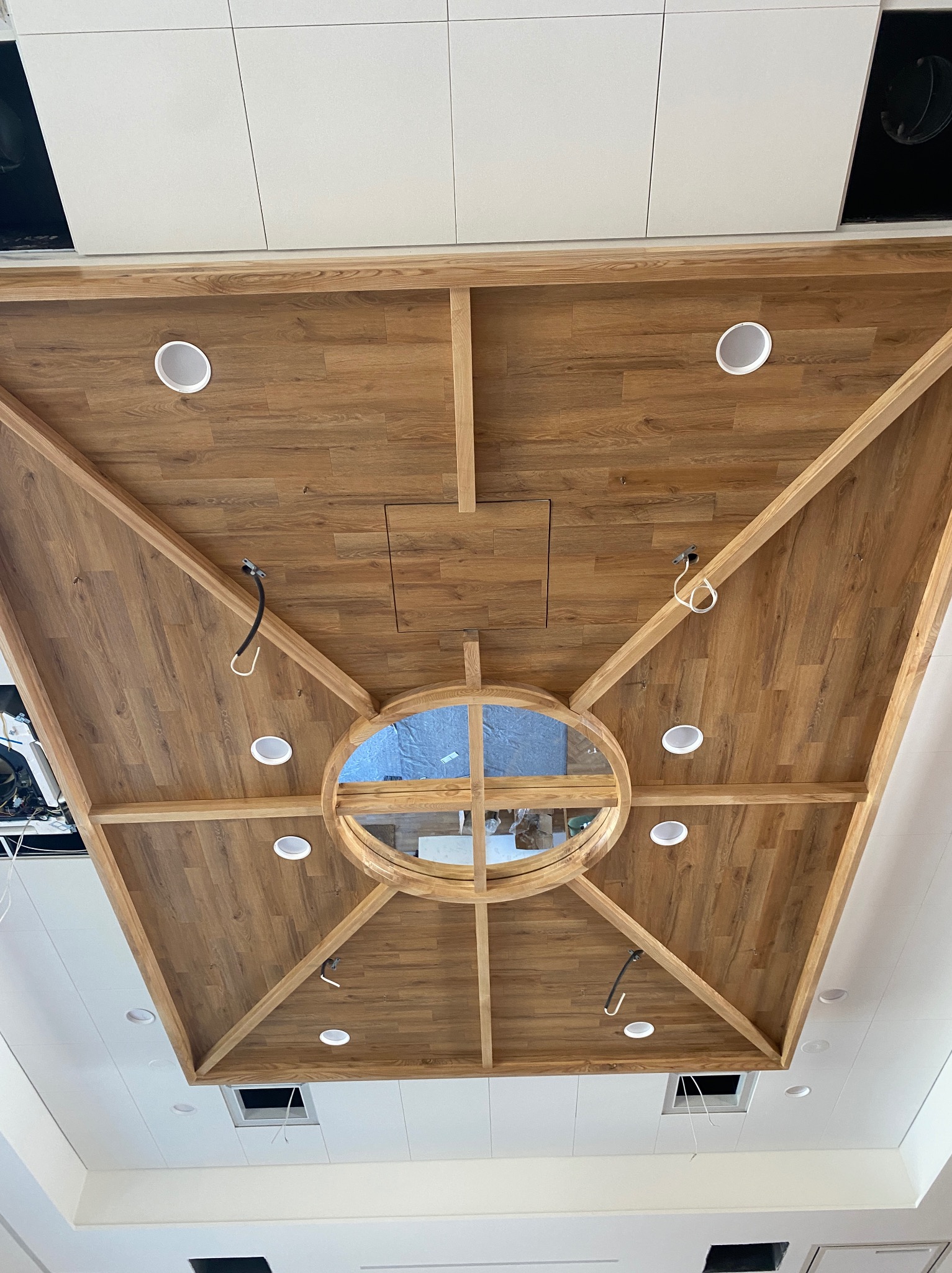 Drewniany sufit kasetonowy z okrągłym świetlikiem i wbudowanym oświetleniem punktowym. Widok z dołu, elementy instalacji elektrycznej widoczne.