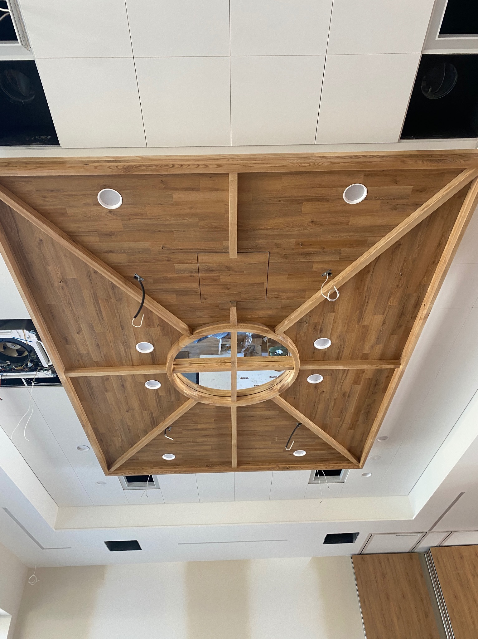 Dekoracyjny sufit podwieszany z drewnianymi panelami i okrągłym otworem w centrum, oświetlony punktowymi lampami, widok z dołu.