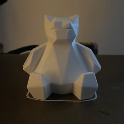 Kamil Kol - Biała, geometryczna figurka kota wykonana w technologii druku 3D, widoczne warstwy druku, na ciemnym tle.