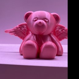 Kamil Kol - Różowy, drukowany w 3D miś z małymi skrzydłami anioła i oczami w kształcie serc, siedzący na jasnej powierzchni pod delikatnym, różowym oświetleniem.