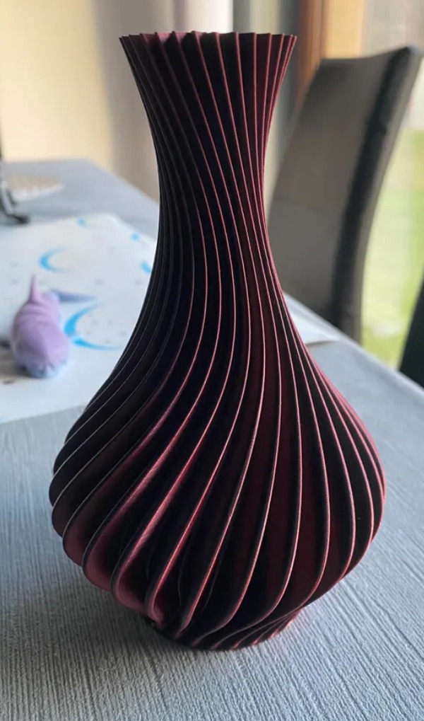 Burgundowa, spiralna waza z drewna lub tworzywa, widoczna na stole z niebieskim elementem dekoracyjnym w tle.