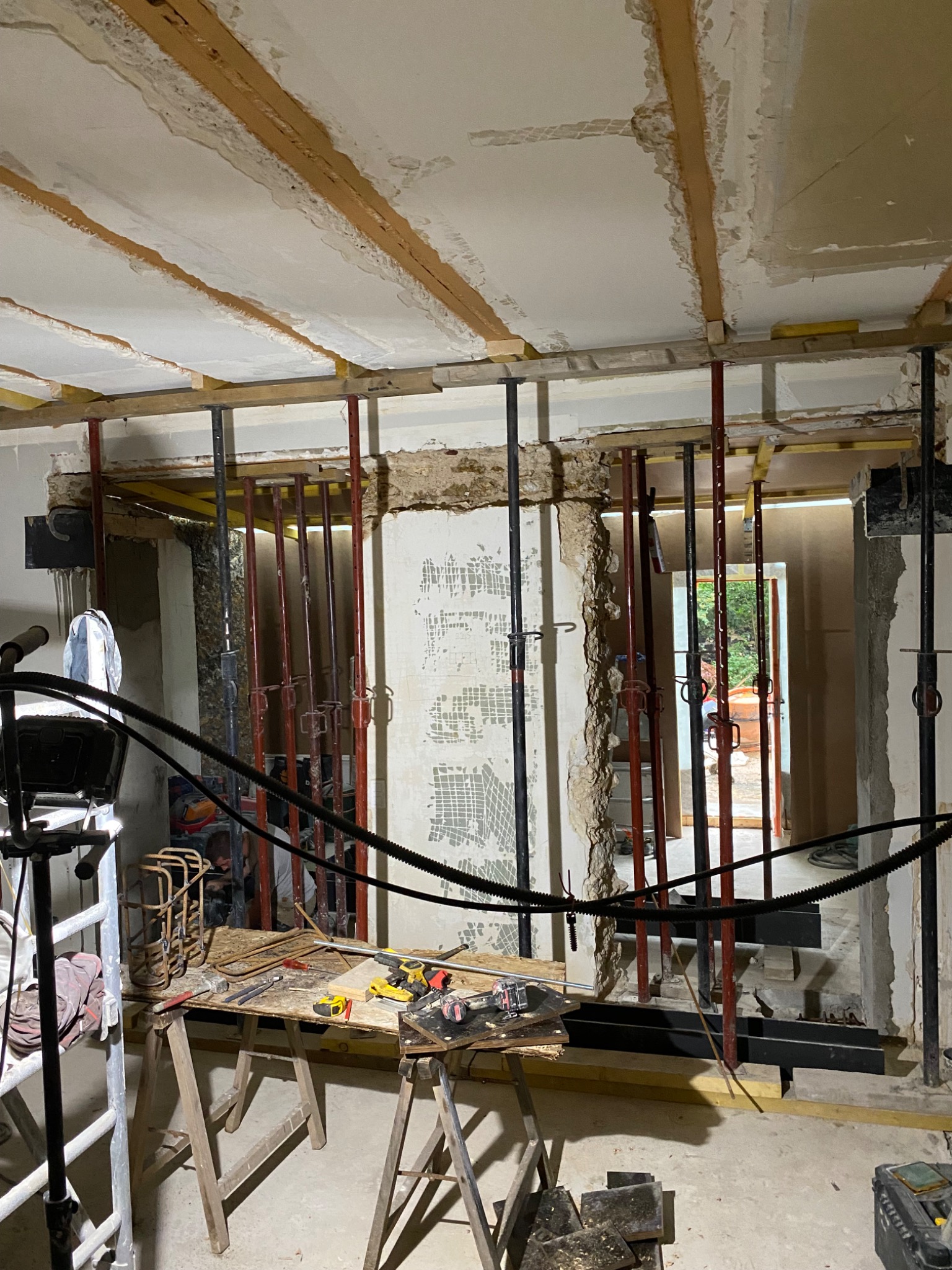 Wnętrze w trakcie remontu: widoczne podpory stropowe, przygotowany sufit pod płytę karton gips, narzędzia na drewnianym stole warsztatowym, częściowo wykończone ściany.