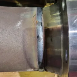 Metalowa rura połączona z kołnierzem za pomocą spawu. Widoczne ślady po spawaniu i oznaczenia na kołnierzu.