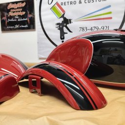 Jarosław Kuśmierek Custom Painting - Części motocyklowe po renowacji: czerwony błotnik z czarnymi pasami, zbiornik paliwa w czerwieni i czerni, z widocznym odbiciem fotografa, na tle plakatu z logiem firmy i certyfikatu
