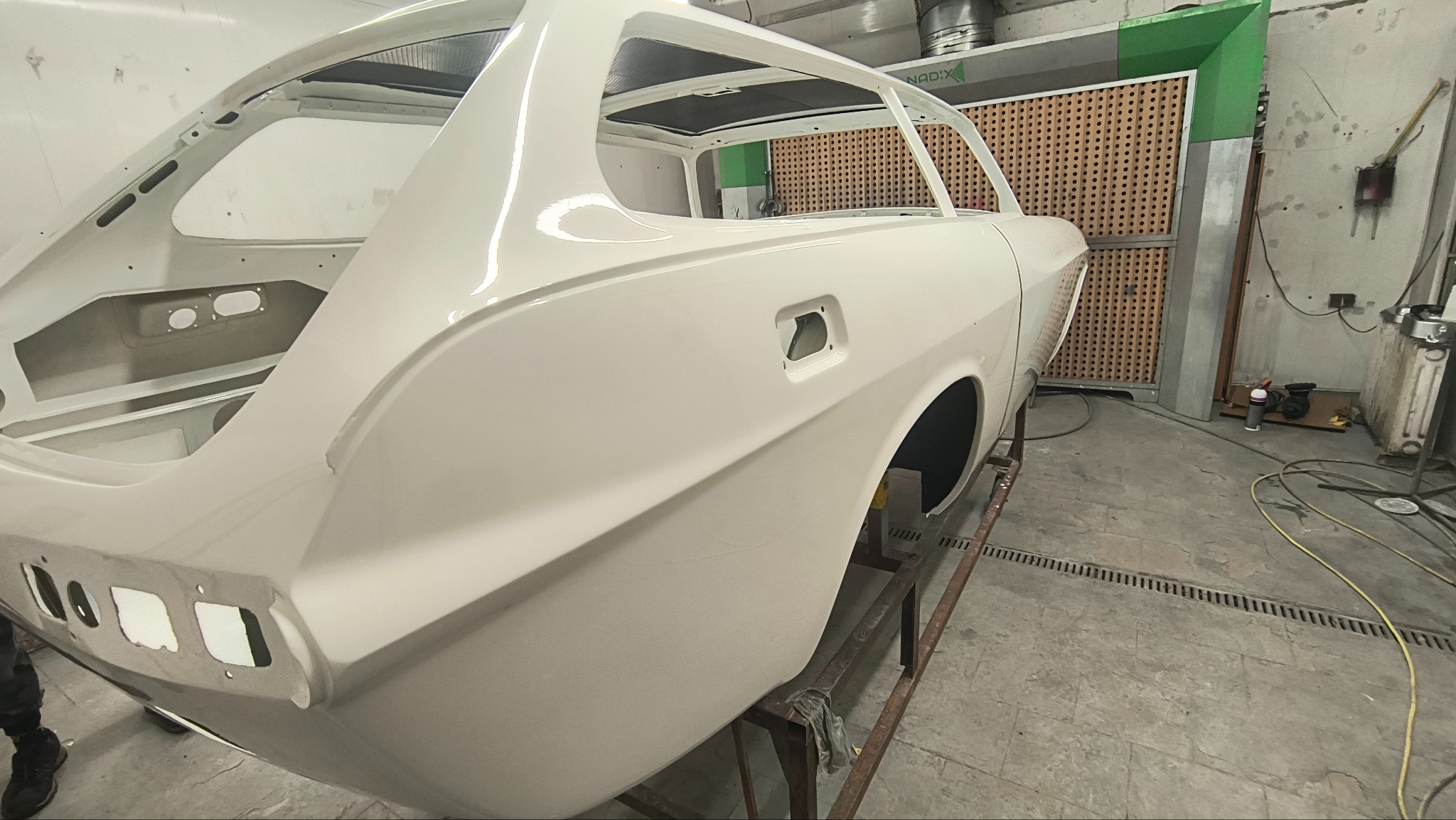Biała karoseria samochodu po lakierowaniu, widoczna w warsztacie. Elementy nadwozia bez szyb i drzwi, przygotowane do dalszego montażu. Świeży lakier z połyskiem.