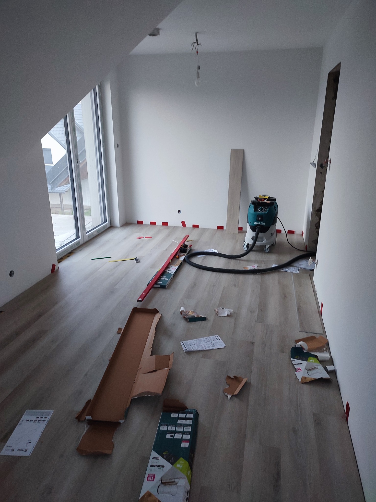 Układanie paneli podłogowych w jasnym pokoju na poddaszu w Grodzisku Dolnym, widoczny odkurzacz przemysłowy i narzędzia.