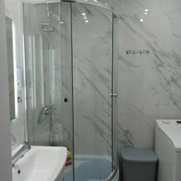 GEBAR HOUSE - kompleksowe wykończenia i remonty - Patryk Gębarowski - Nowoczesna łazienka po remoncie: kabina prysznicowa z chromowanymi elementami, umywalka z szafką, marmurowe płytki na ścianach, pralka i szary kosz na pranie.