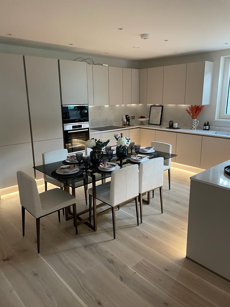 Nowoczesna kuchnia z beżowymi szafkami, czarnym szklanym stołem nakrytym do uroczystej kolacji i drewnianą podłogą z subtelnym oświetleniem LED przy podłodze.