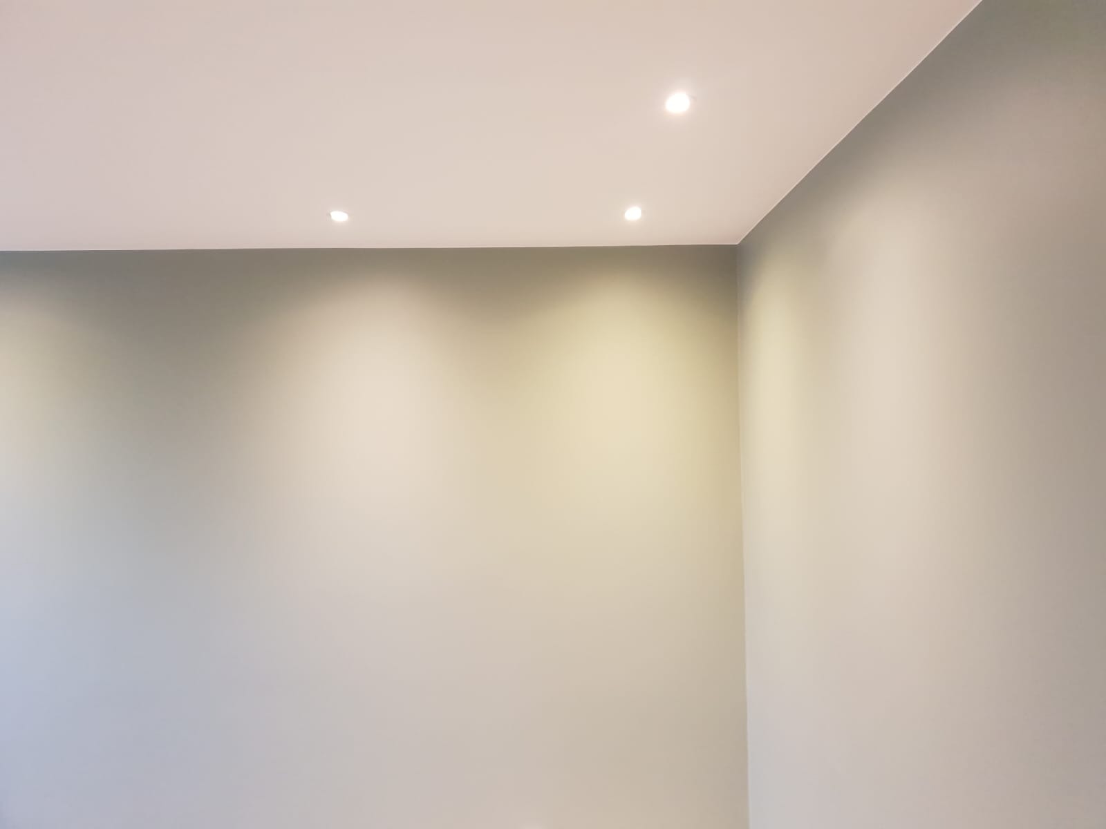 Pomalowane na szaro ściany w rogu pokoju z trzema wbudowanymi punktowymi lampami sufitowymi.