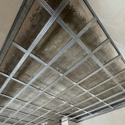 MR. WHITE Marek Ryborz - Metalowa konstrukcja sufitu podwieszanego z widocznymi elementami mocującymi, surowy stan, przygotowanie do montażu płyt. Widok z dołu.