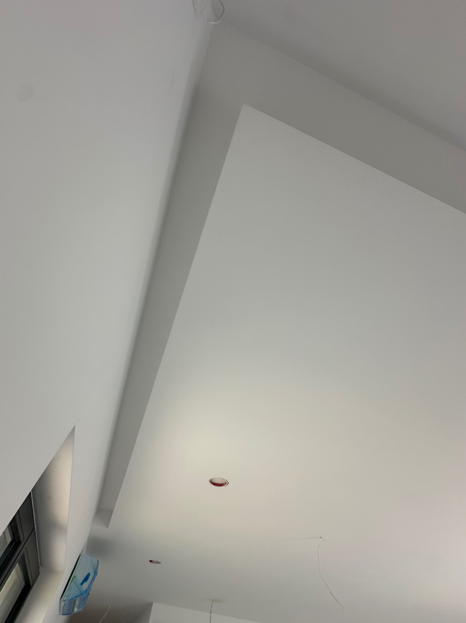 Białe, gładkie wykończenie sufitu pod skosem, z widocznymi otworami na oświetlenie. Minimalistyczny design, świeżo po remoncie. Widok z dołu.