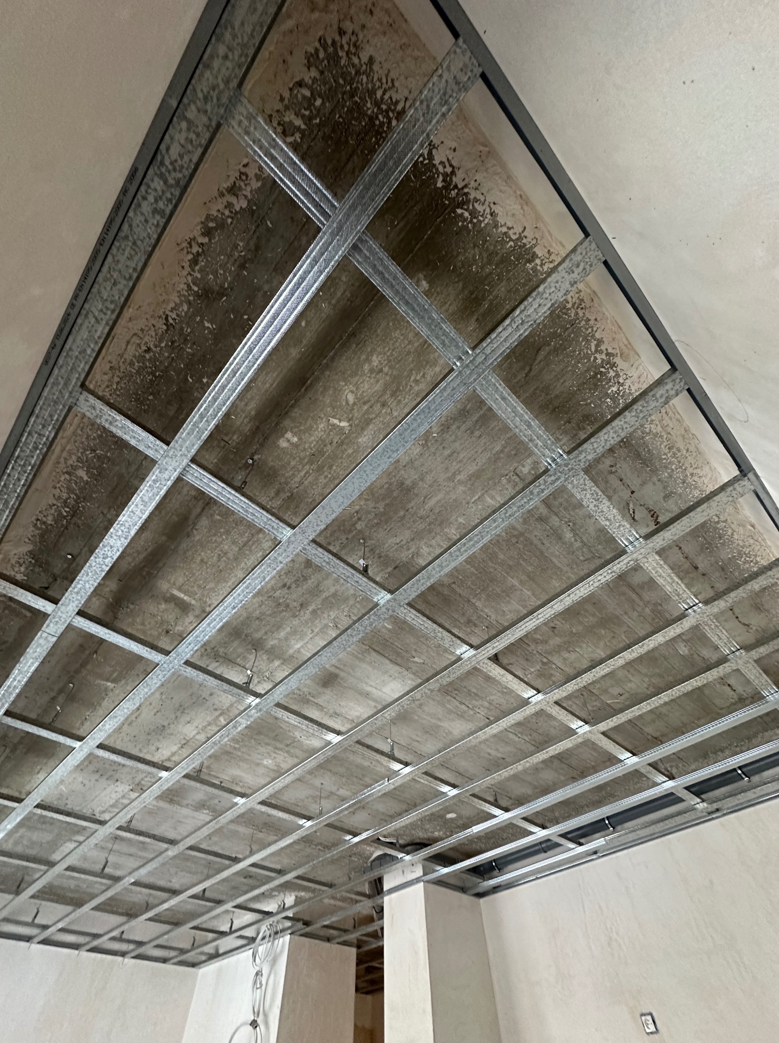 Metalowa konstrukcja sufitu podwieszanego z widocznymi elementami mocującymi, surowy stan, przygotowanie do montażu płyt. Widok z dołu.